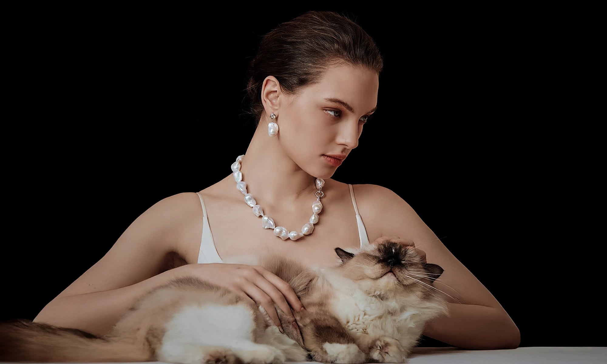 Woman wearing a baroque pearl necklace with a cat